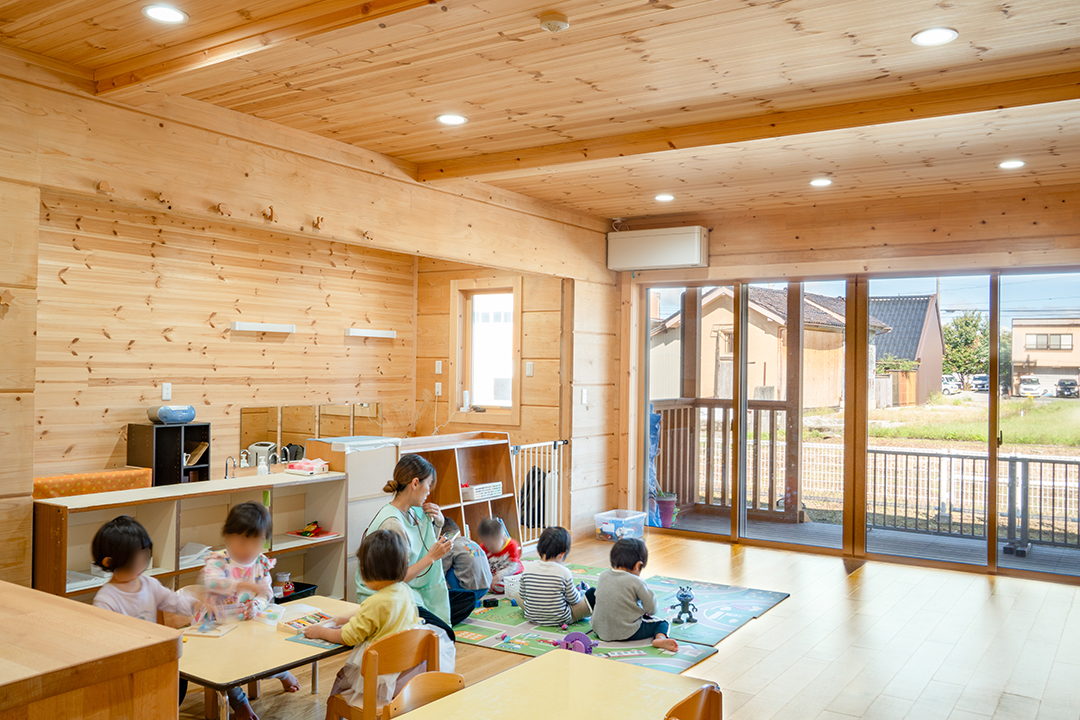 木に囲まれた明るい保育室で遊ぶ園児たち